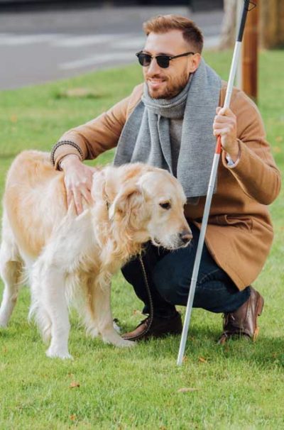 Smiling blind man with walking stick petting guide dog on lawn